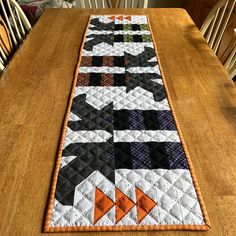 the table runner is made with black, orange and white quilts on top of a wooden table