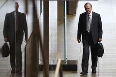 a man in a suit and tie walking down the hall with his luggage behind him