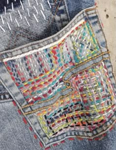 the back pocket of a pair of jeans with colorful stitching on it and an open zipper