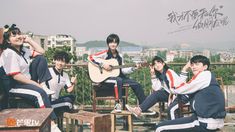 group of young people sitting on wooden chairs with guitar in hand and buildings in the background