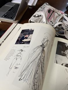 an open book with drawings on it sitting on a table next to a laptop computer