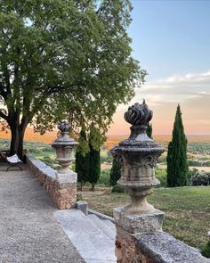 an outdoor area with stone pillars and trees in the background, overlooking a valley at sunset