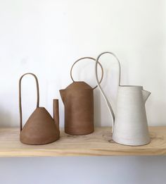 three clay pots are sitting on a wooden shelf next to a white jug and a brown pitcher