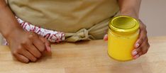 a person holding a yellow jar on top of a wooden table