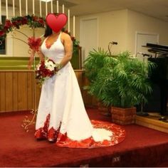 a woman in a white dress standing on a stage with flowers and a red heart