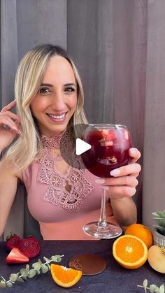 a woman holding up a wine glass with fruit around it