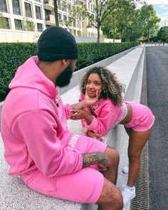 a man and woman sitting on the ground next to each other wearing pink sweat suits