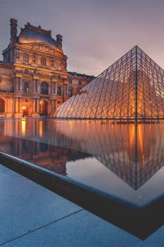 a large glass pyramid in front of a building with a reflection on the water at night