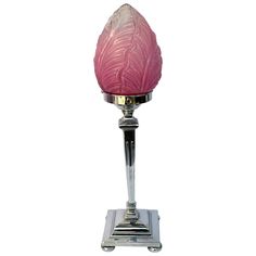 a pink glass candle holder sitting on top of a metal stand with a white background