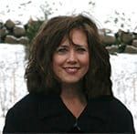 a woman with long hair smiling in front of snow covered ground and trees behind her