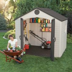 a woman sitting in a wheelbarrow next to a shed with gardening supplies on it