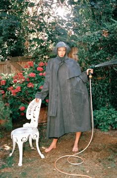 a woman standing next to a white chair with a hose in her hand and an umbrella on the ground