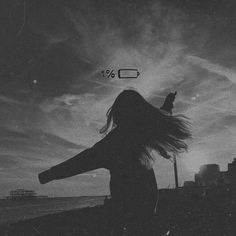 a woman standing on the beach with her hair blowing in the wind and an overcast sky