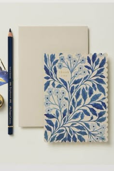 a blue and white flowered notebook next to a pair of scissors, pencils and a pocket watch