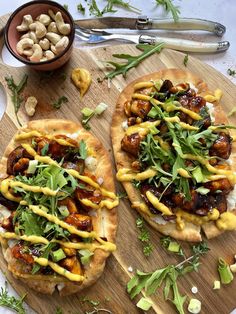 two flatbread pizzas topped with cheese and greens on a cutting board next to a bowl of nuts