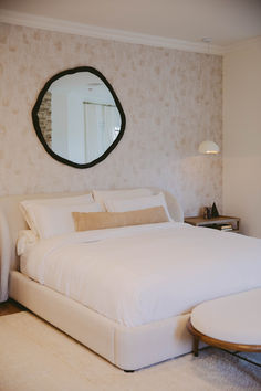 a large white bed sitting under a round mirror