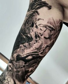 a man's arm covered in black and grey ink with birds flying over it