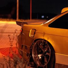 a yellow car is parked on the side of the road at night with its lights on