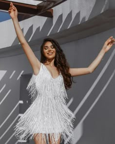 a woman in a white fringe dress posing for a photo with her arms up and legs spread out