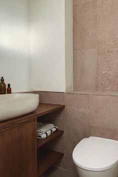 a white toilet sitting next to a wooden cabinet in a bathroom on top of a tiled floor