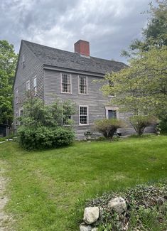 an old gray house sitting on top of a lush green field