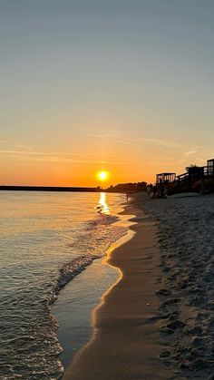 the sun is setting over the water at the beach