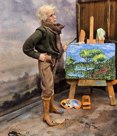 a doll is standing next to an easel with a painting on it