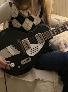 a woman sitting on top of a bed holding a black and white electric guitar in her lap