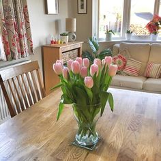 a vase filled with pink tulips sitting on top of a wooden table next to a couch