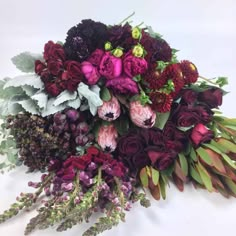 a bunch of flowers sitting on top of a white table next to green leaves and purple flowers