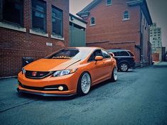 an orange car parked in front of a brick building on the side of a road