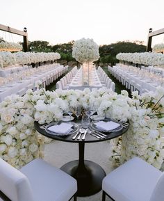 a table set up with white flowers and place settings in front of rows of chairs