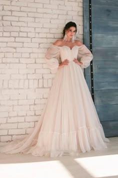 a woman standing in front of a white brick wall wearing a dress with long sleeves