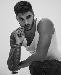 a man with tattoos sitting down and holding his hand to his chin, looking at the camera