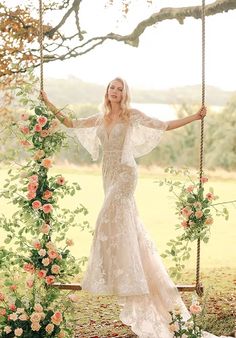 a woman in a wedding dress on a swing with flowers and greenery around her