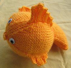 an orange knitted fish sitting on top of a white bed sheet with blue eyes