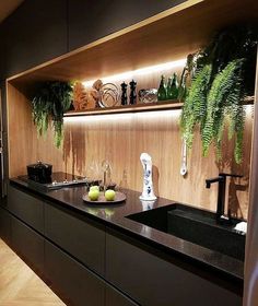 a kitchen with black counter tops and wooden shelves filled with green plants, vases and bottles