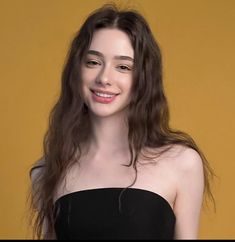 a woman with long brown hair wearing a strapless black dress and smiling at the camera