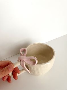 a hand is holding a spoon with a pink bow on it and the bowl has been made out of clay