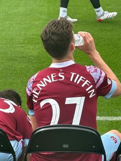 a man drinking water from a bottle while sitting on the sidelines at a soccer game