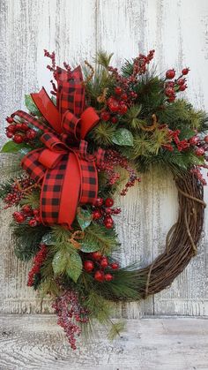 a wreath with red and black plaid bow hanging on a white wall next to a wooden door