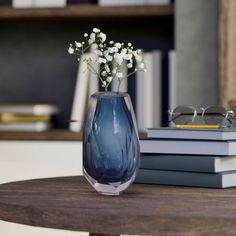 a blue vase sitting on top of a wooden table next to books and eyeglasses