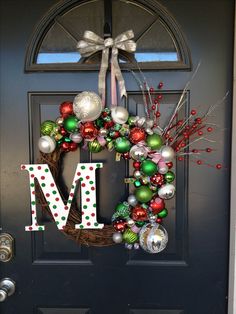 a christmas wreath with ornaments hanging on the front door and letter m in the middle