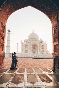 a man and woman standing in front of a building with an archway leading into it