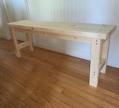 a wooden bench sitting on top of a hard wood floor next to a white wall