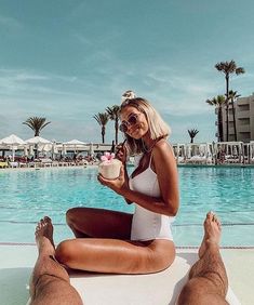 a woman sitting on the edge of a swimming pool holding a cupcake in her hand