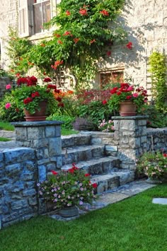 a stone wall with flowers in pots on it and steps leading up to the house