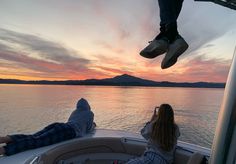 two people are sitting on the back of a boat watching the sun set over water