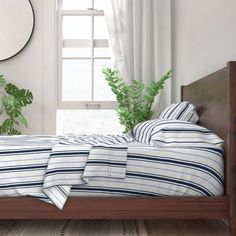 a bed sitting next to a window with a plant in the corner on top of it