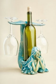 there is a wine bottle and two glasses next to the mermaid figurine on the table